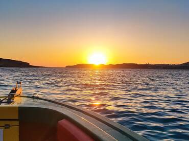A stunning sunset view from the bow of a boat, showcasing the tranquil waters and distant coastline — perfect for evening cruises.