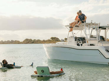A group enjoys a relaxing day on the water, with one couple perched on the boat and others floating nearby — perfect for summer fun and social gatherings.