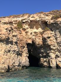 A stunning view of a coastal cave surrounded by rocky cliffs and clear turquoise waters, perfect for exploring and sightseeing during boat trips.