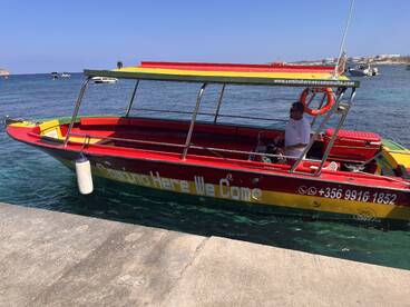 A vibrant speedboat named 'Comino Here We Come' docked in clear waters, showcasing its colorful design and ready for adventure in Malta.