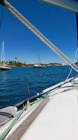 A scenic view of a sailboat navigating through calm waters, showcasing the beauty of the coastline and nearby vessels.