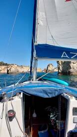 A scenic view from the deck of a sailboat, showcasing the vessel's sail and the rocky coastline in the background — perfect for sailing enthusiasts and coastal adventures.