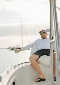 A man relaxes on the bow of a boat, enjoying a drink and the serene waters — perfect for a laid-back day on the water.