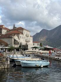 A picturesque view of docked boats in a charming harbor, with historic buildings and mountains in the background, perfect for exploring coastal destinations.
