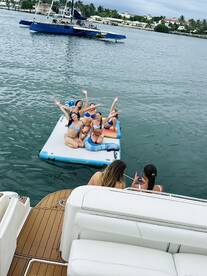 A lively group of friends enjoys a fun day on the water, posing on a floating mat while soaking up the sun — perfect for summer celebrations and memorable outings.