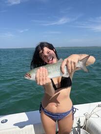 A joyful moment captured as a young woman proudly holds up her catch while fishing on a boat in the ocean, showcasing the thrill of a successful day on the water.