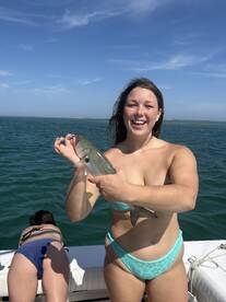 A joyful moment captured as a woman proudly holds up her catch while fishing on a boat, showcasing the thrill of ocean adventures.