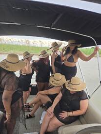 A lively group of friends celebrates together on a pontoon boat, showcasing their stylish hats and enjoying a fun day on the water.