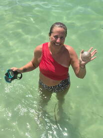 A woman enjoys a sunny day in the water, holding a sand dollar and snorkeling gear — a perfect moment of beach fun and exploration.
