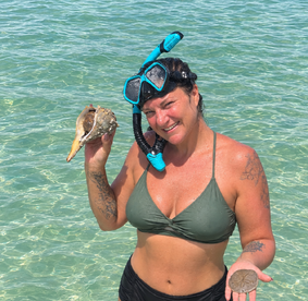 A woman enjoys snorkeling in clear waters, proudly holding a shell she found — a perfect moment of adventure and exploration in a tropical paradise.