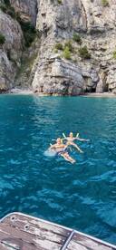 Two friends enjoy a refreshing swim in crystal-clear waters near a stunning rocky coastline, perfect for summer adventures.