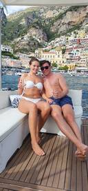 A couple enjoys cocktails on a luxurious boat with stunning coastal scenery in the background, perfect for romantic getaways or special celebrations.
