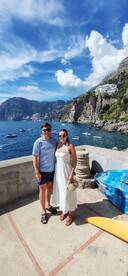 A couple poses for a photo with stunning coastal scenery in the background, capturing a memorable moment on their trip.