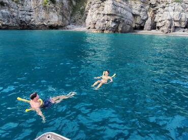 A couple enjoys a refreshing swim in crystal-clear waters, surrounded by stunning rocky cliffs — a perfect moment for snorkeling and relaxation.