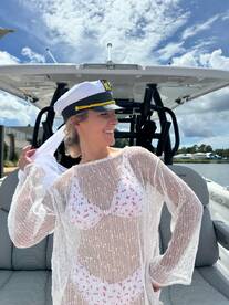 A joyful woman poses in a captain's hat on a boat, showcasing a fun day on the water — perfect for summer adventures and celebrations.