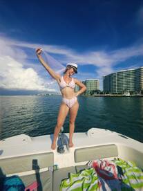 A joyful woman celebrates on the bow of a boat, showcasing a fun day on the water under a bright blue sky — perfect for summer adventures.