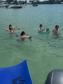 A lively group enjoys a fun day in the water, floating with drinks and pool noodles — the perfect way to relax and socialize on a sunny day.