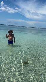 A man enjoys a refreshing drink while standing in the clear waters, showcasing a perfect beach day under the sun.