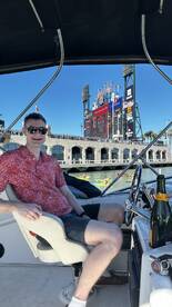A man enjoys a relaxing moment on a boat with champagne, overlooking the vibrant cityscape and kayakers in the background — a perfect day on the water.