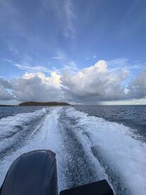 A dynamic view from the back of a boat, showcasing the wake and a distant island under a dramatic sky — perfect for capturing the essence of a boating adventure.