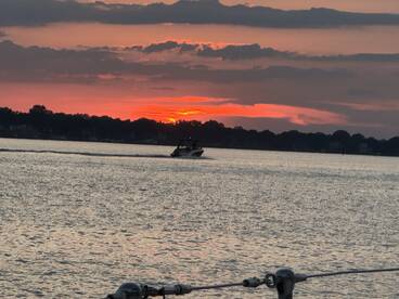 A serene sunset view over the water with a boat cruising in the foreground, capturing the tranquil beauty of evening on the lake.