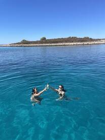 Two friends celebrate in the crystal-clear waters, clinking their drinks in a joyful moment — perfect for summer adventures and memorable getaways.