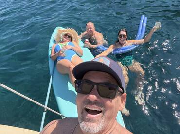 A lively group enjoys a sunny day on the water, relaxing on a paddleboard and sipping cocktails — a perfect moment of summer fun.