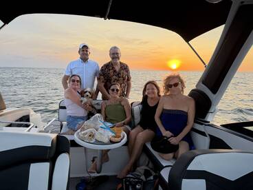 A joyful group of friends enjoys a sunset cruise on a boat, capturing a perfect moment with laughter and a furry companion.