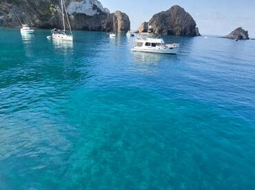 A serene view of multiple yachts anchored in crystal-clear waters, surrounded by stunning rocky formations — ideal for exploring beautiful coastal destinations.