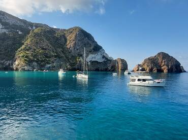 A serene view of several yachts anchored in crystal-clear waters, surrounded by stunning rocky cliffs — a perfect destination for boating enthusiasts.