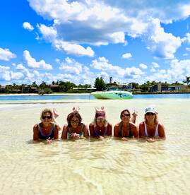 A fun group of friends enjoys a sunny day at the beach, playfully posing in the shallow water with a boat anchored nearby — perfect for memorable summer outings.