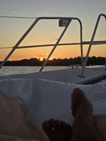 A serene sunset view from a boat, with feet resting on the deck, creating a perfect atmosphere for relaxation on the water.