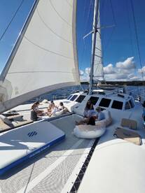 A group of friends relaxes on the deck of a catamaran under a sunny sky, enjoying a perfect day on the water.