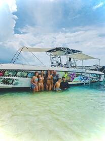 A joyful group of friends and family poses in shallow water next to the 'Cool Runnings' powerboat, capturing a fun day on the water.