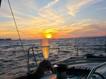 A hand raises a glass of champagne against a stunning sunset backdrop on a yacht, perfect for romantic celebrations or sunset cruises.