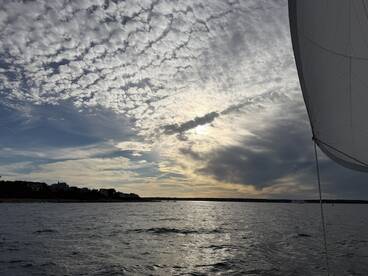 A serene view of a sailboat's sail against a dramatic sky at sunset, showcasing the beauty of a peaceful sailing experience.