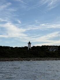 A picturesque view of a lighthouse standing tall against a backdrop of blue skies and lush greenery, perfect for capturing the essence of coastal adventures.