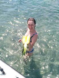 A joyful moment captured as a woman holds a pineapple while swimming in clear waters, showcasing the fun and vibrant atmosphere of a tropical getaway.