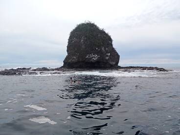 Snorkelers explore the waters near a striking rock formation, showcasing the beauty of ocean adventures and marine life.