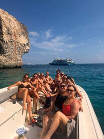 A lively group of women enjoys a fun day on the water, celebrating together on a boat near stunning coastal cliffs — perfect for bachelorette parties or group outings.