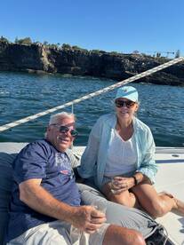 A couple enjoys drinks while relaxing on a boat, with stunning rocky cliffs in the background — perfect for a serene day on the water.