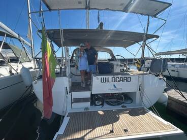 A cheerful couple poses aboard the yacht 'WILDCARD,' capturing a moment of joy at the marina — perfect for romantic getaways or sailing adventures.