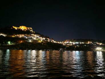 A stunning night view of a harbor illuminated by city lights and a historic castle, creating a picturesque backdrop for evening boat trips.