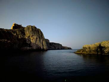 A serene nighttime view of rugged cliffs reflecting in calm waters, showcasing the natural beauty of the coastline — perfect for evening boat tours.