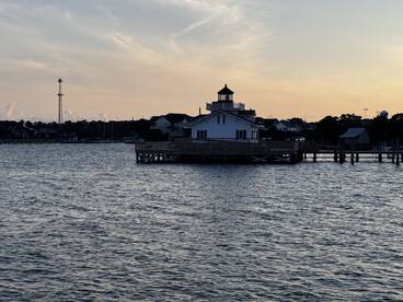 A scenic view featuring a lighthouse and waterfront structures at sunset, capturing the tranquil atmosphere of the area.