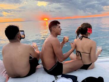 A group enjoys a stunning sunset on a yacht, sipping cocktails and capturing the moment — perfect for memorable celebrations on the water.