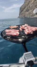 A close-up of a grill on a boat, featuring a selection of meats sizzling over the flames — perfect for a delicious barbecue experience on the water.