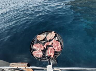 A grill loaded with fresh cuts of meat sits on the edge of a boat, perfect for a delicious barbecue experience on the water.