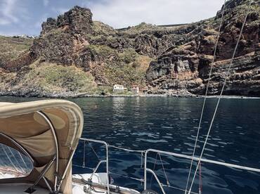 A serene view from the deck of a boat, showcasing rugged cliffs and a quaint coastal house, perfect for capturing the beauty of nature while sailing.