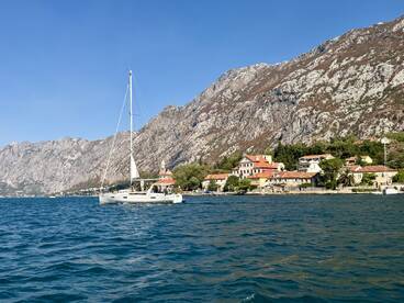 A picturesque sailboat navigates the serene waters near a charming coastal village, framed by majestic mountains — an ideal setting for sailing enthusiasts.